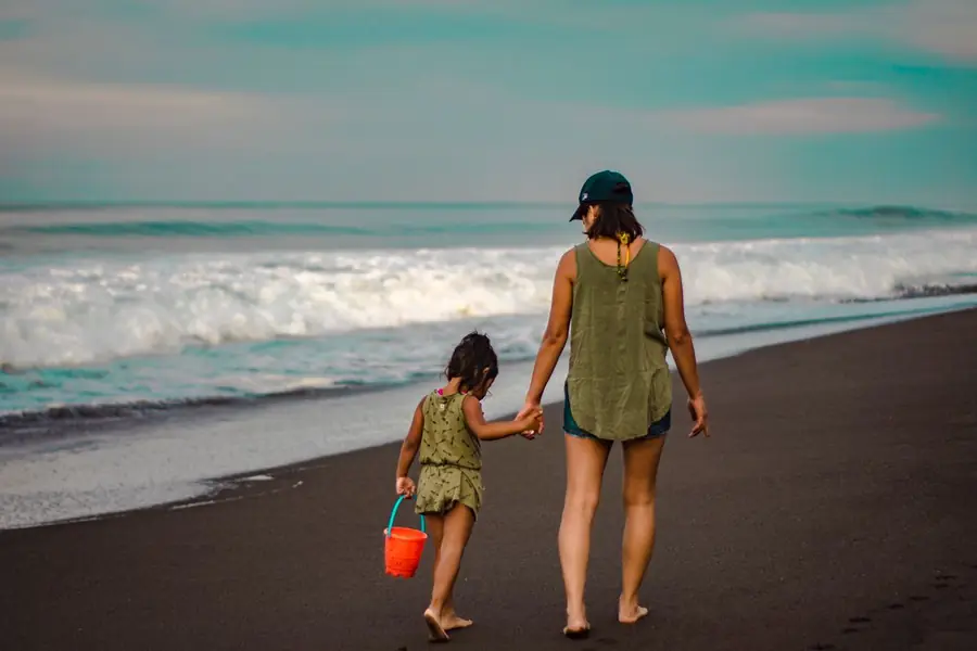 A helper and child walking hand in hand along a beach