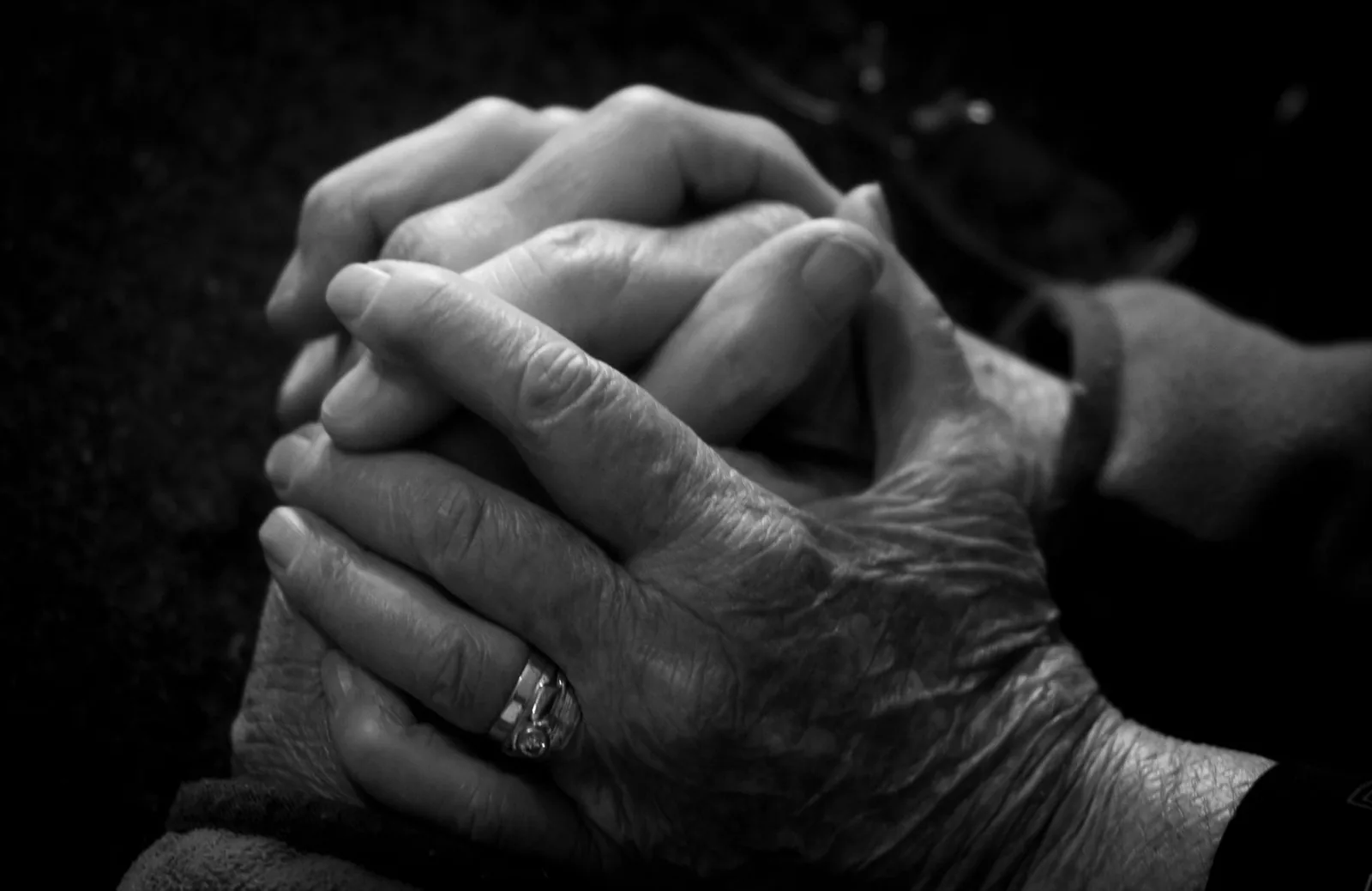 Black-and-white close-up of an older person's hands clasped with a younger person's hands