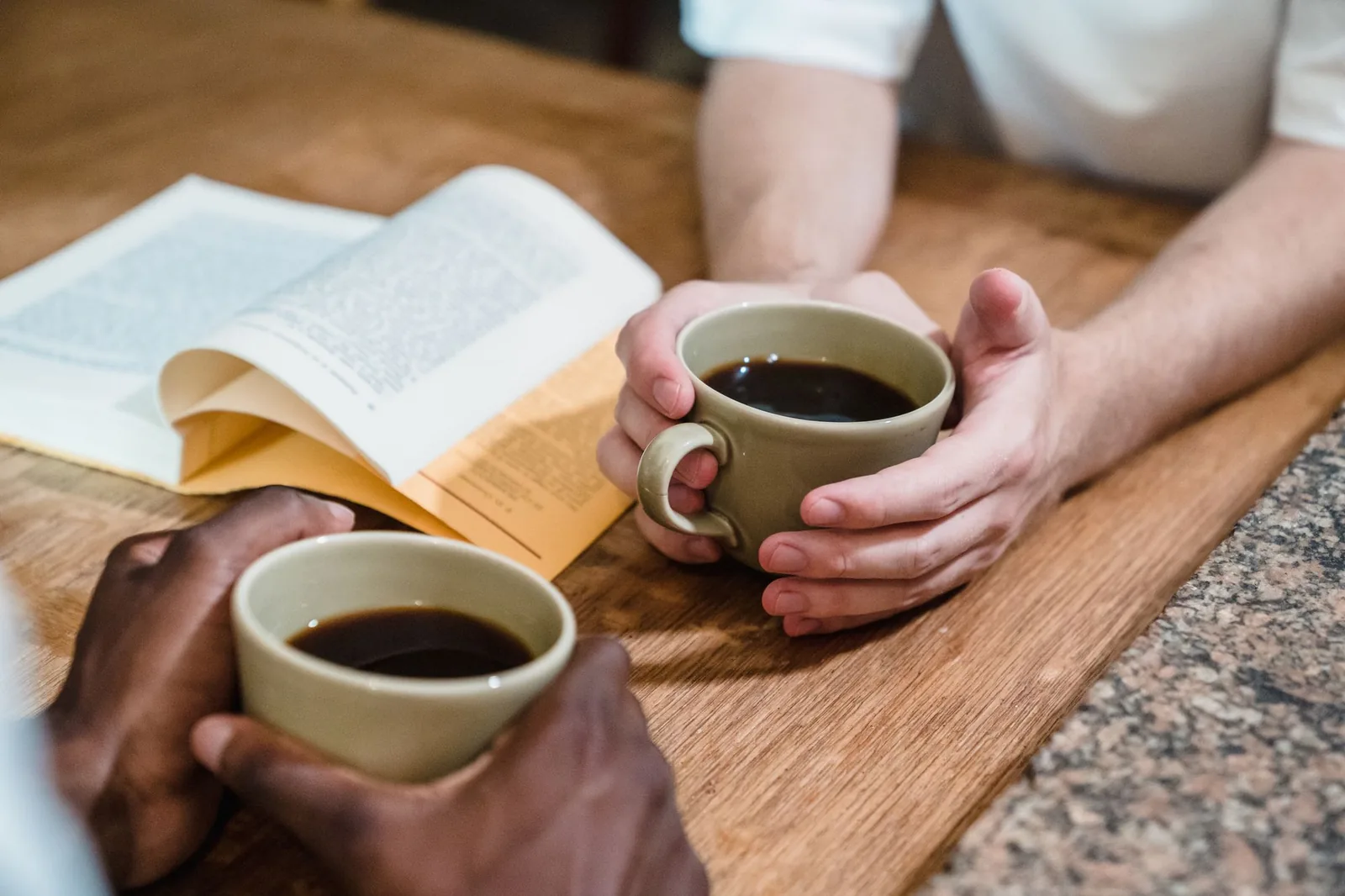 Two people holding cups of coffee across a wooden table