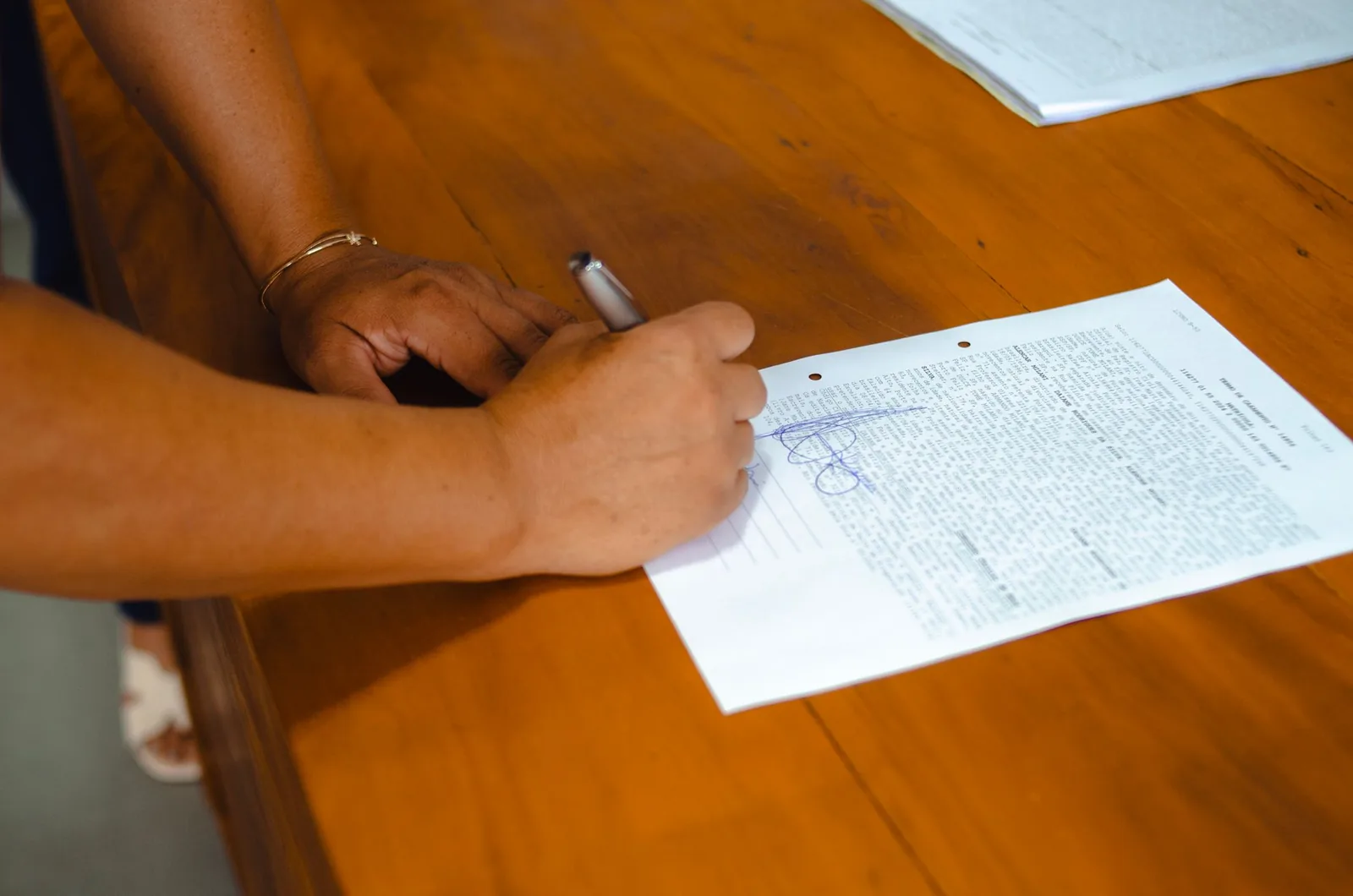 Close-up of hands signing a document with a pen at a wooden table