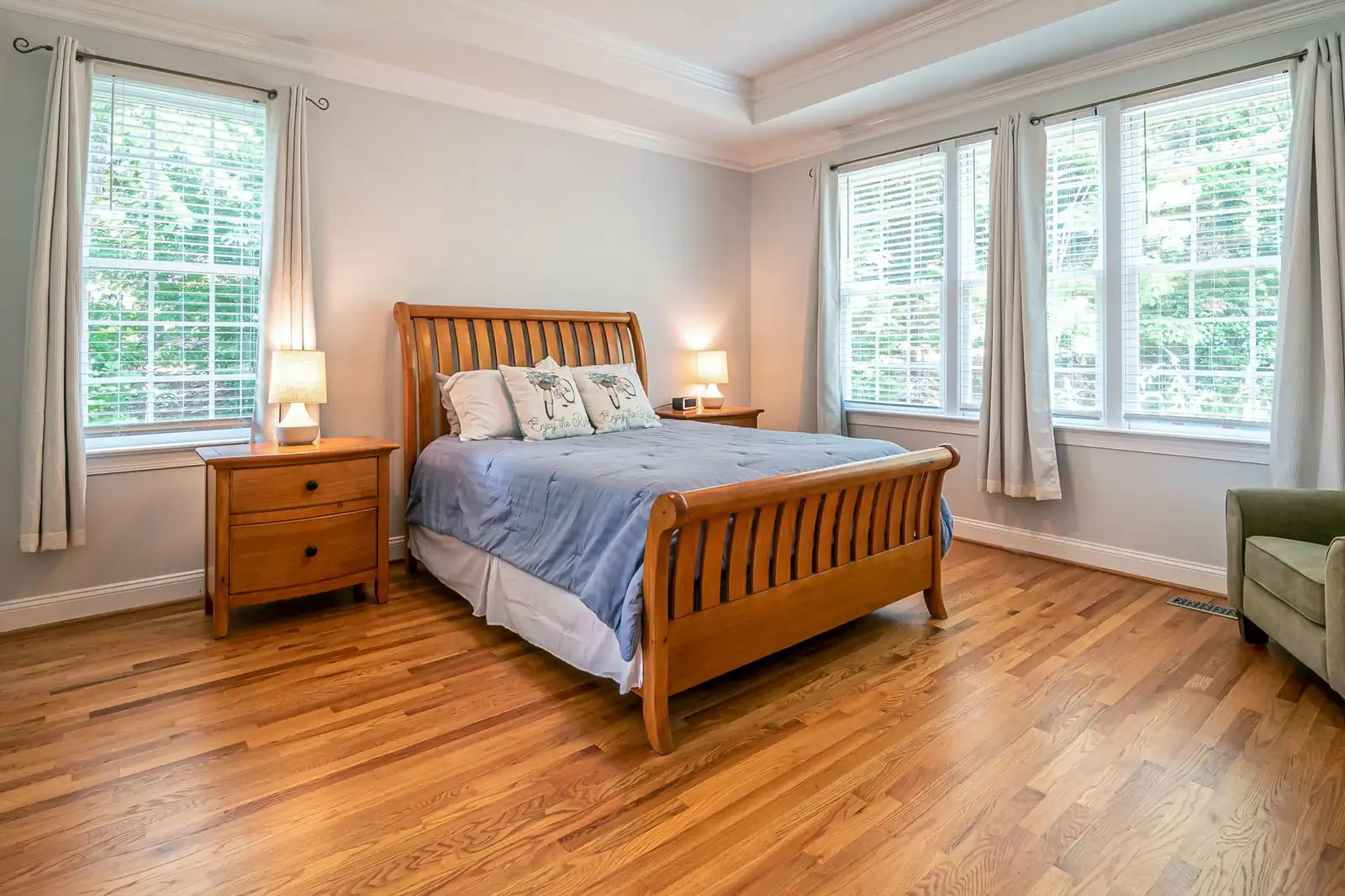 A bright bedroom with a wooden bed and large windows letting in daylight