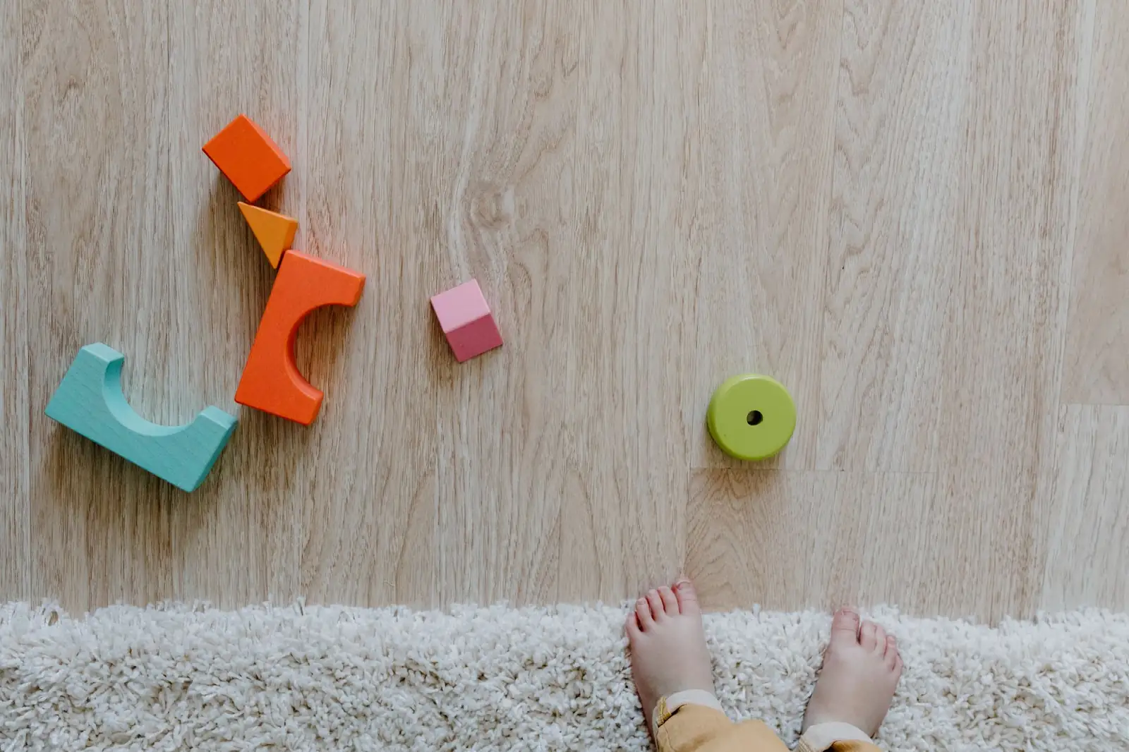 Colourful wooden toy blocks on a floor beside a small child's bare feet