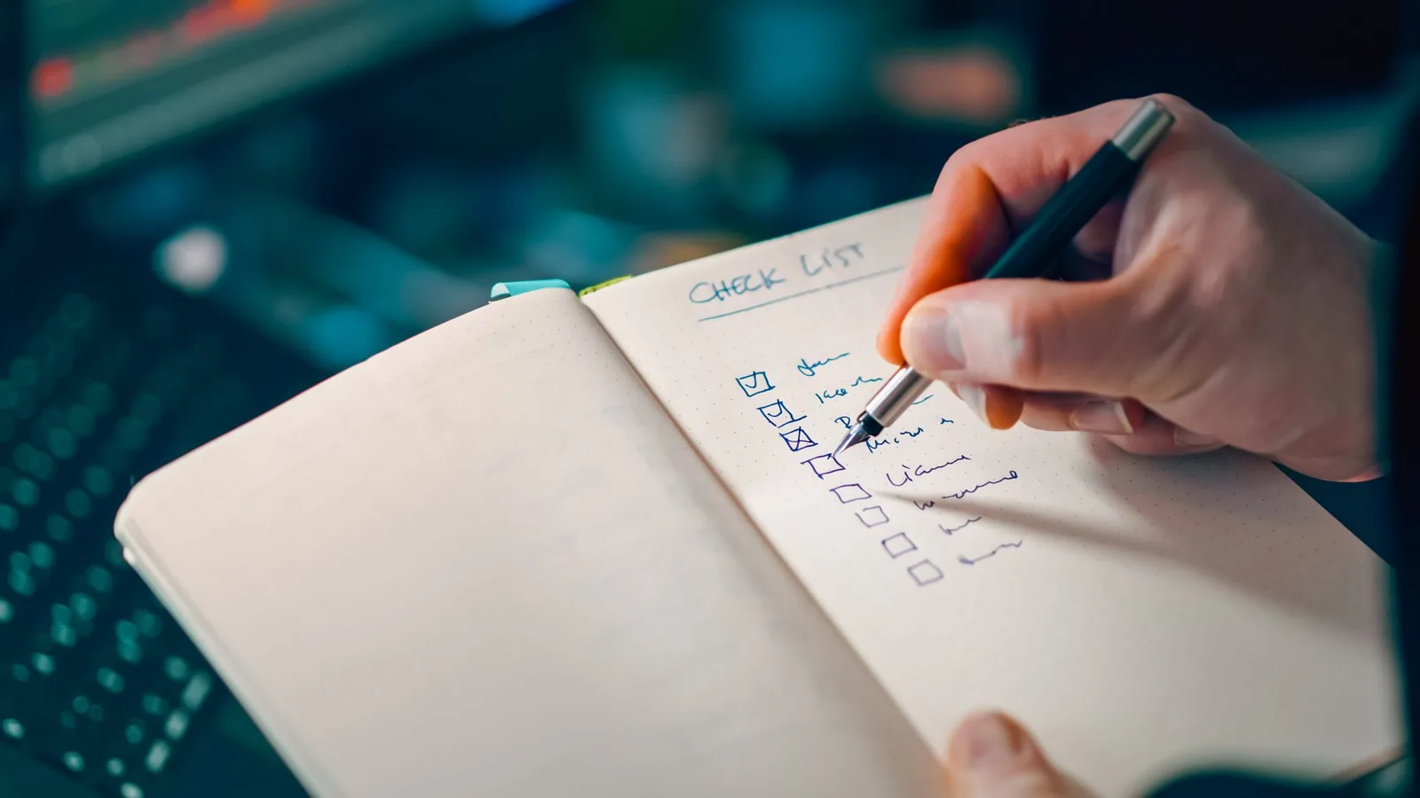 A hand ticking items on a handwritten checklist in a notebook