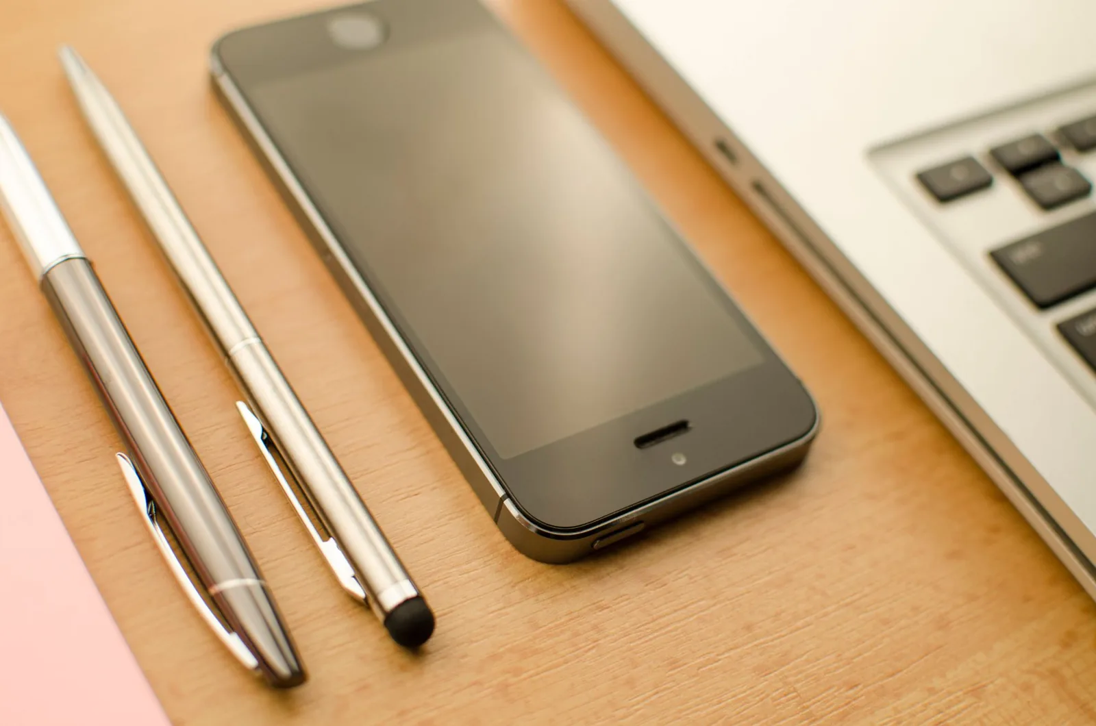 A smartphone, two pens and a laptop on a desk